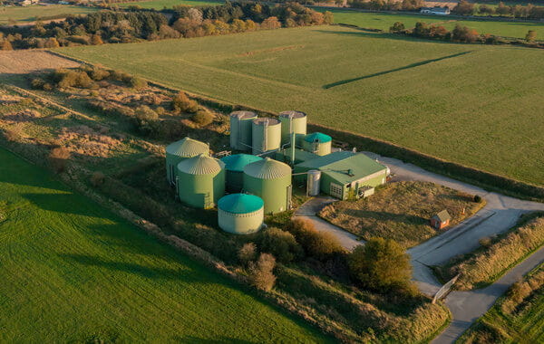 Eine Biogasanlage mit mehreren grünen Fermentern und Betriebsgebäuden, umgeben von landwirtschaftlichen Flächen.