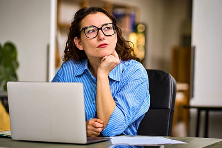 Frau vor einem Laptop überlegt