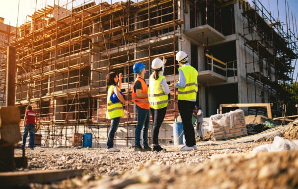 Personen in Warnwesten befinden sich auch einer Großbaustelle und schauen auf Neubau