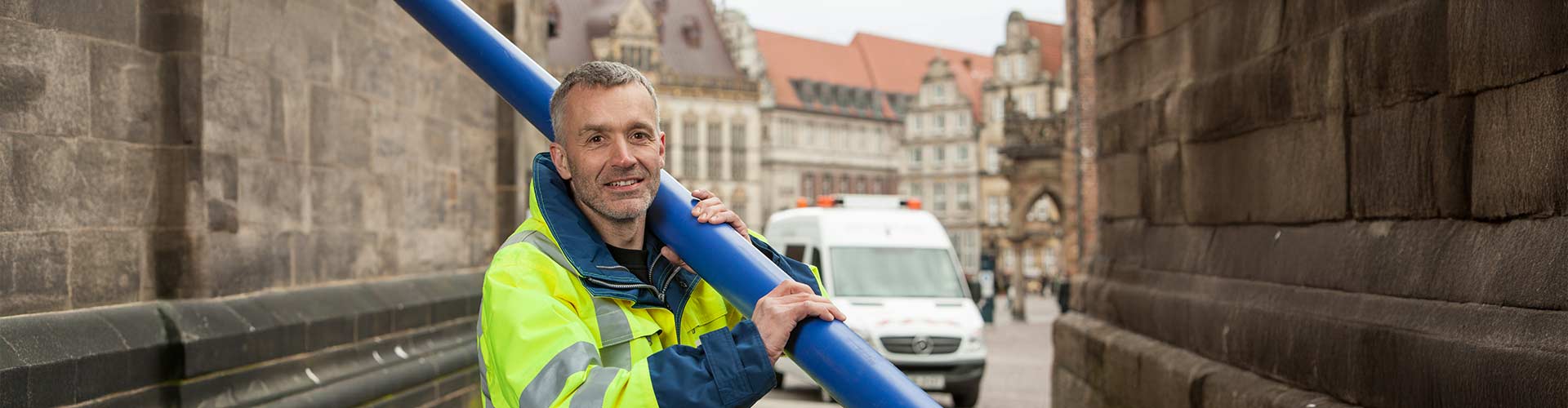 Ein Mitarbeiter trägt ein blaues Rohr und lächelt in die Kamera