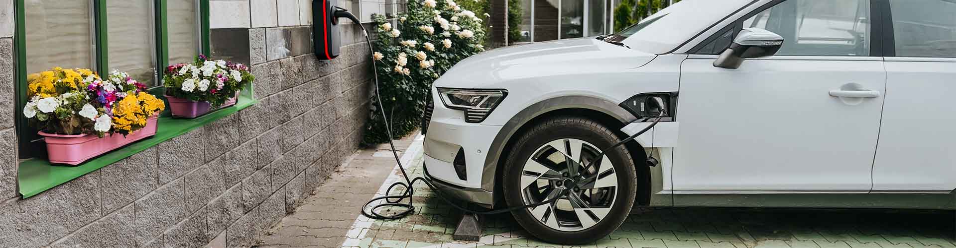 Ein weißes E-Auto lädt an einer Ladestation vor einem Privathaus