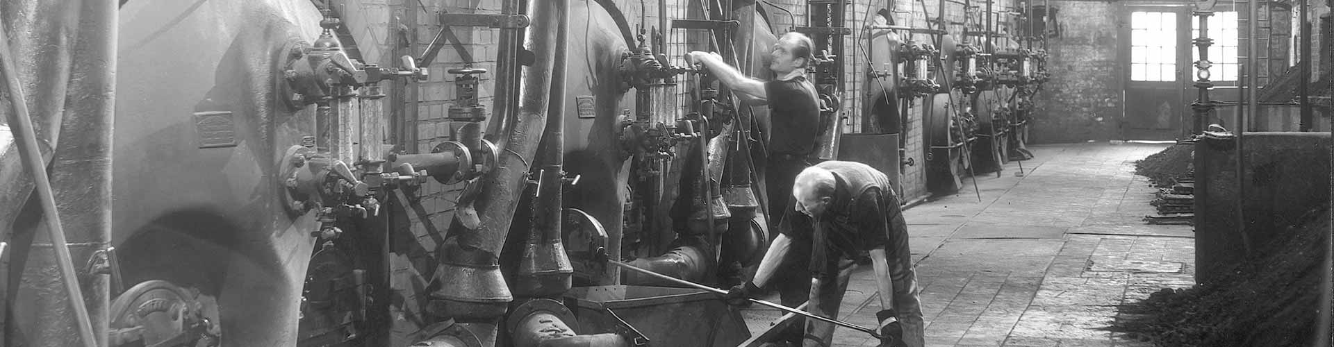 Ein historisches Foto in schwarz und weiß von zwei Mitarbeitenden im Heizkraftwerk