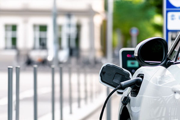 Ein weißes E-Auto lädt am Straßenrand an einer öffentlichen Ladesäule