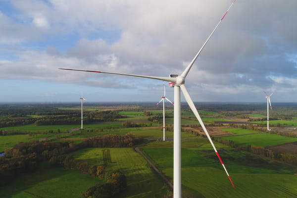 Mehrere Windkraftanlagen stehen bei sonnigem Wetter in einer grünen Landschaft