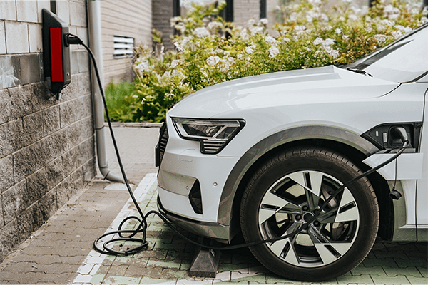 Weißes E-Auto lädt an einer Wallbox vor einem modernen Haus mit Garten