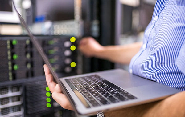 Person hält Laptop und stellt etwas an blinkenden Servern ein