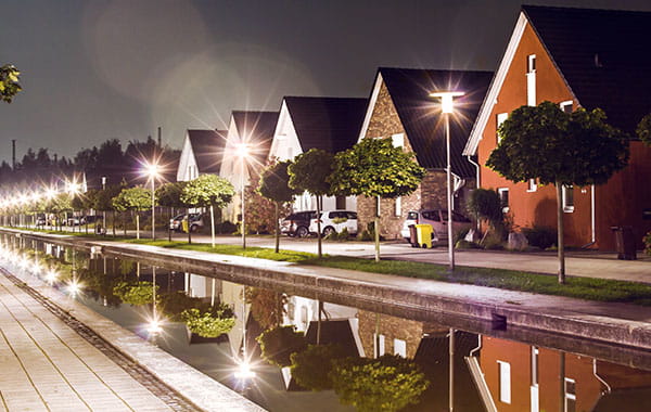 Nachtaufnahme einer beleuchteten Siedlung mit Spiegelung der Straßenlichter im Fluss.