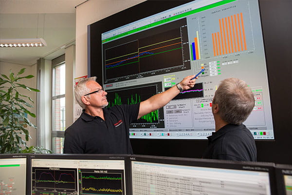 Zwei Mitarbeitende besprechen Statistiken an einem großen Bildschirm 