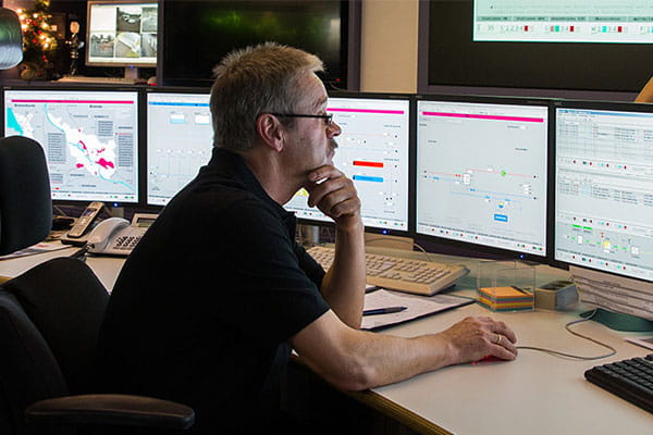 Ein Mitarbeiter in der Schaltzentrale sitzt an einem Schreibtisch mit mehreren Bildschirmen