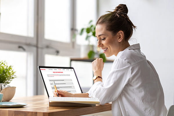 Eine Frau sitzt am Laptop, hat das FAQ für Einspeiser geöffnet und notiert sie sich etwas