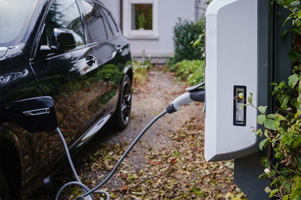schwarzes Elektroauto in einer Einfahrt angeschlossen an eine weiße Ladesäule