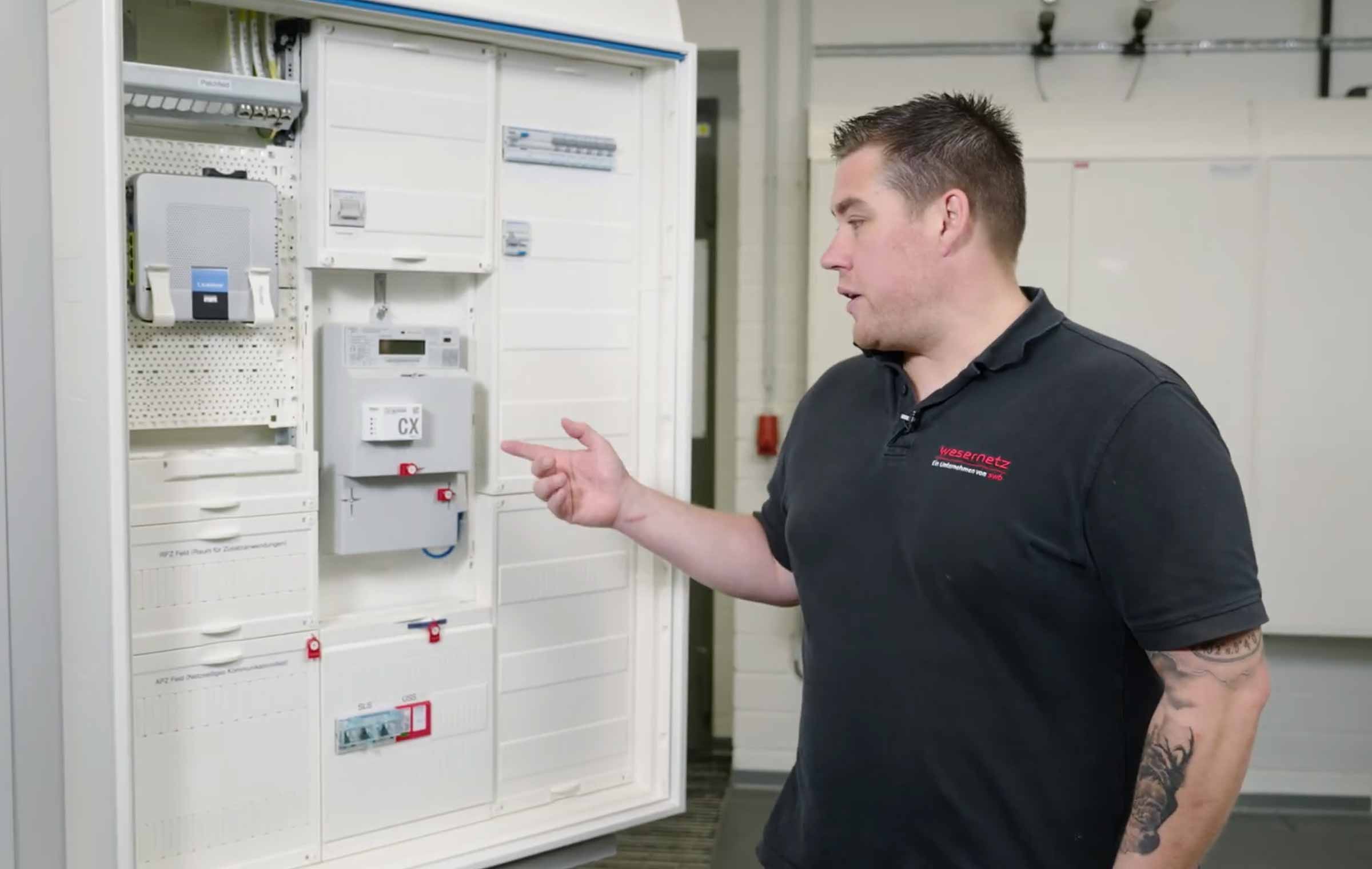 Ein Mitarbeiter zeigt auf einen weißen Zählerschrank. Es ist ein moderner Zählerplatz
