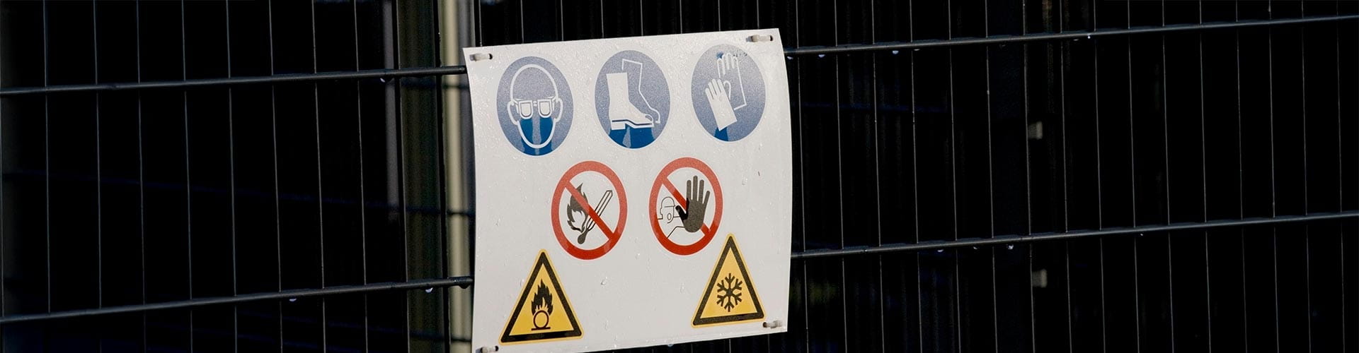 Ein Schild mit Arbeitssicherheitshinweisen ist an einem Baustellenzaun montiert