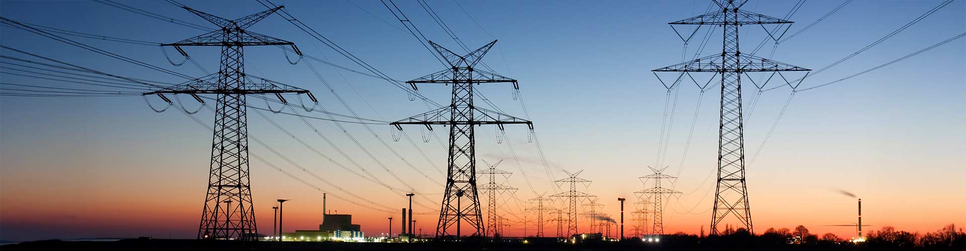Ein Stromnetz mit drei Strommasten während eines Sonnenaufgang