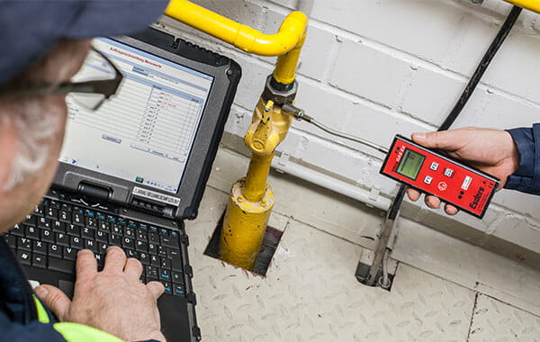 Ein Messgerät ist an ein Gasrohr angeschlossen, auf einem Laptop überprüft ein Mitarbeiter  die Erdgaswerte 