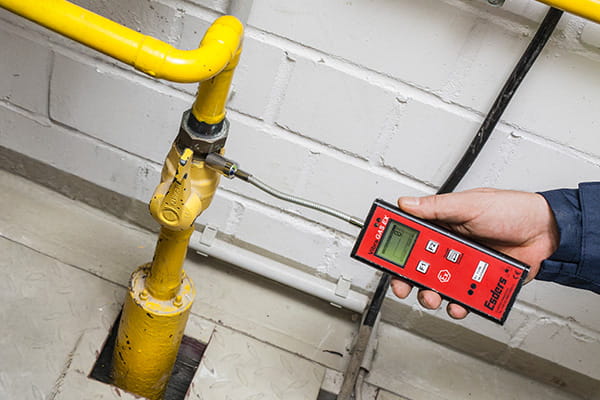 Eine Person misst an einer gelben Gasleitung den Druck