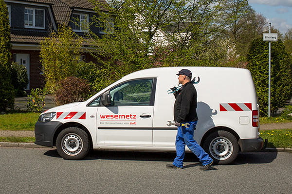 Ein Monteur läuft mit Werkzeug an seinem wesernetz Fahrzeug vorbei