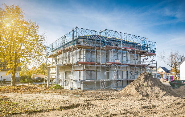 Rohbau-Baustelle mit Sandhaufen vor einem von Gerüst umschlossenen Haus
