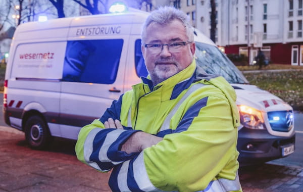 Entstörungsdienst-Mitarbeiter mit verschränkten Armen vor Wesernetz-Sprinter mit Blaulicht