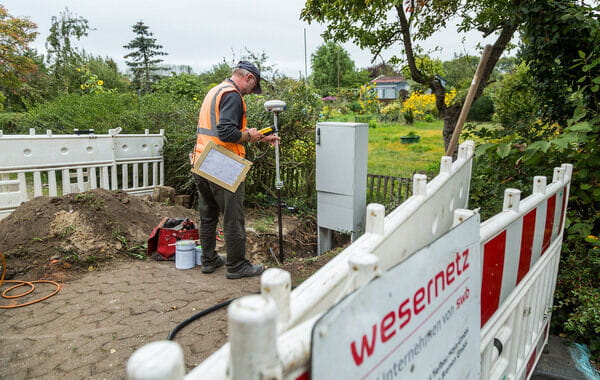 Ein Arbeiter in Warnweste führt Vermessungsarbeiten an einer Baustelle durch, die mit Absperrungen von „wesernetz“ gesichert ist.