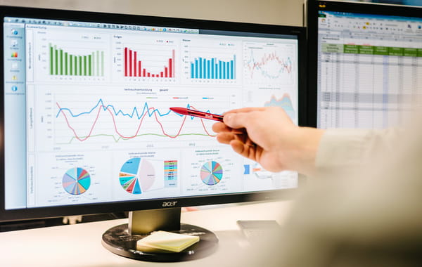 Ein Bildschirm zeigt Diagramme, eine Hand deutet mit einem roten Stift darauf.
