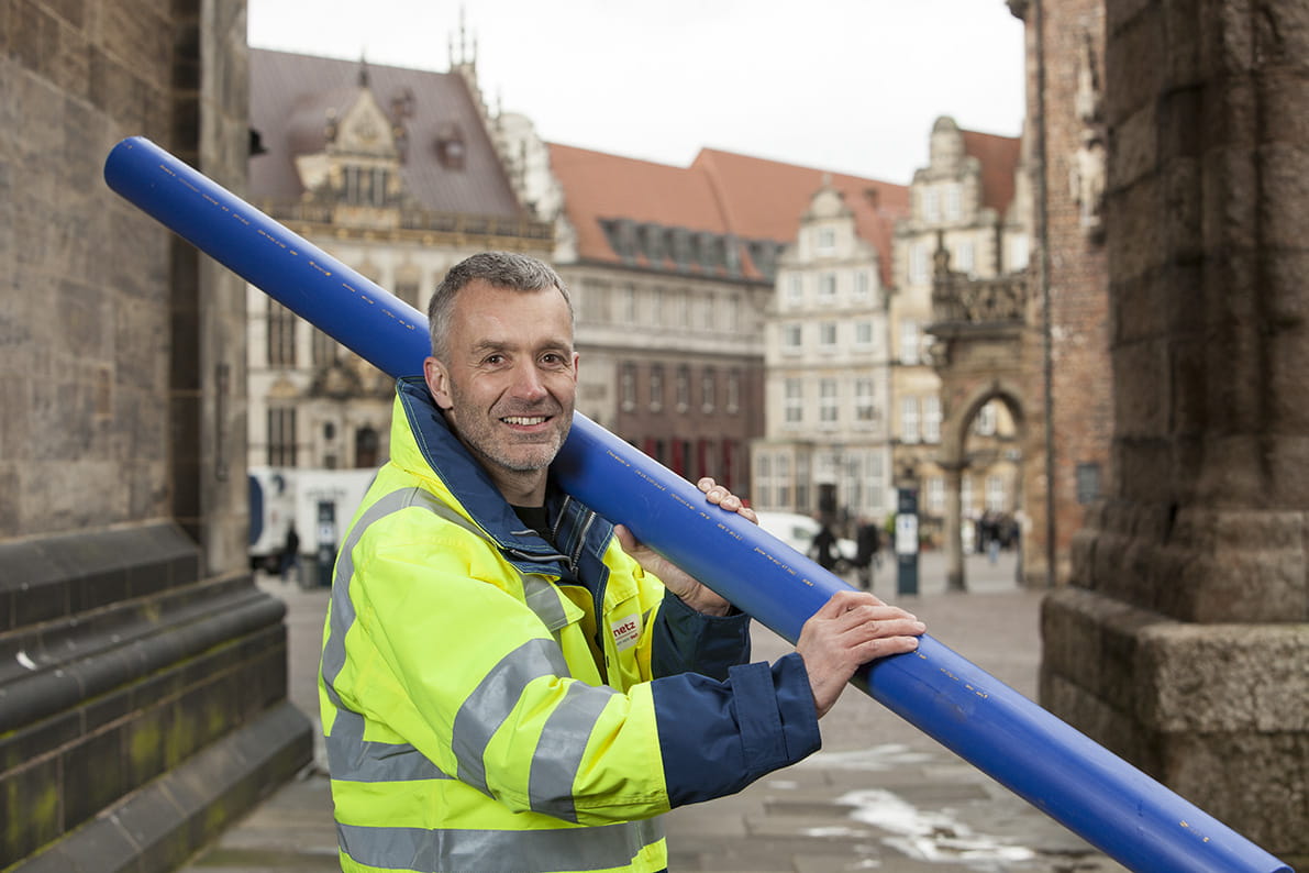 Wesernetz-Mitarbeiter in Schutzjacke trägt blaues Rohr in der Bremer Innenstadt