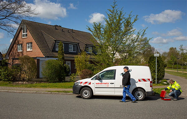 Wesernetz-Wagen vor einem Haus, ein Mitarbeiter läuft mit Werkzeug, ein anderer packt einen Werkzeugkoffer aus