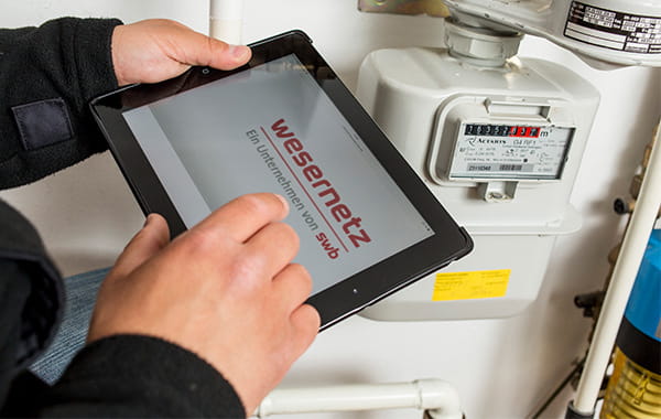 Person hält Tablet mit geöffneter Wesernetz-Webseite, Stromzähler im Hintergrund
