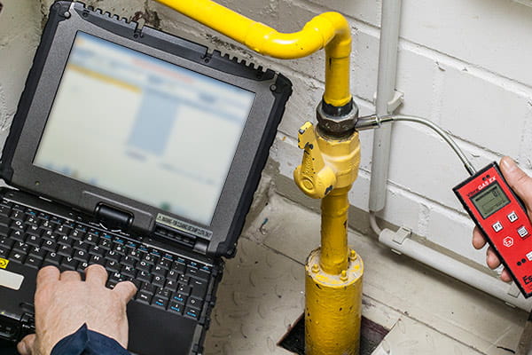 Ein Messgerät ist an ein Gasrohr angeschlossen, auf einem Laptop wird damit die  Erdgassicherheit überprüft